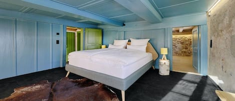 A bedroom with a large bed, a wooden floor, a cowhide rug, and a stone wall.