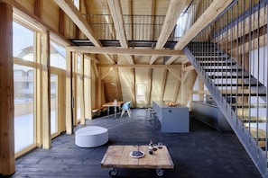 An interior with a high ceiling, wooden beams, a staircase, a dining area, and a kitchen. - Holiday apartment with 2 bedrooms (Löffingen)
