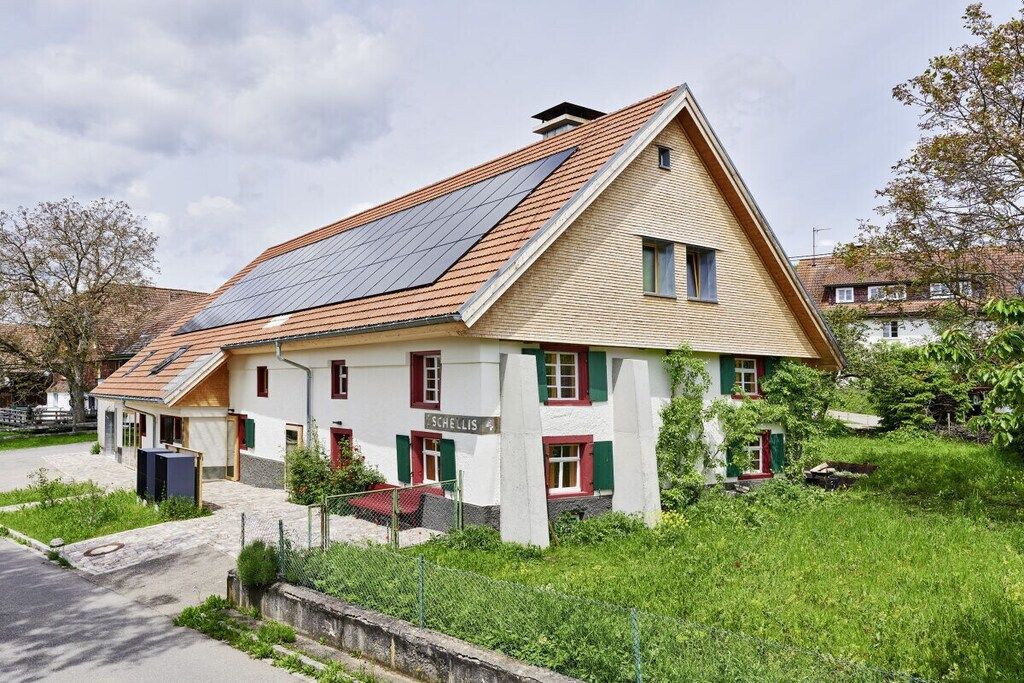 Ein zweigeschossiges Gebäude mit einem geneigten Dach und Solaranlagen, mit einem Schild, auf dem 'SCHELLIS' steht.