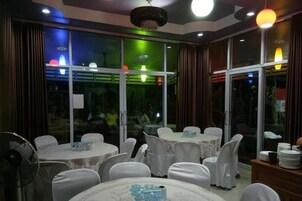 Uma sala de jantar com mesas redondas, cadeiras e um ventilador.