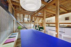 A spacious interior with a high ceiling, exposed wooden beams, a staircase, and a dining area with a blue table. - Holiday apartment with 3 bedrooms (Löffingen)