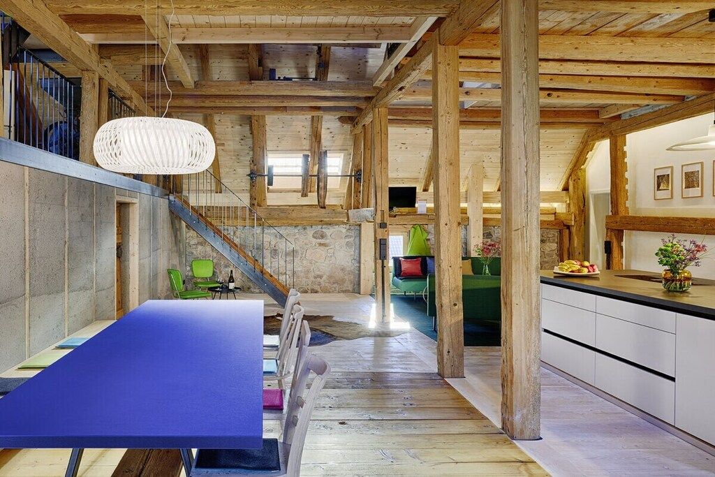 Ein geräumiger Raum mit großem Tisch, Stühlen, einer Treppe und einer Küchenzeile.