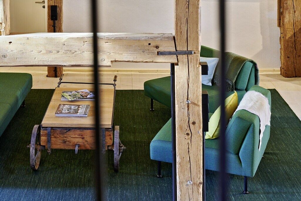 Ein Zimmer mit einem grünen Sofa, einem Holztisch und einer rustikalen Holzbalkenkonstruktion.
