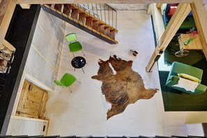 Ein Zimmer mit einer großen Tierfelldecke, grünen Stühlen, einer Treppe und einem Holztisch mit einer Vase.