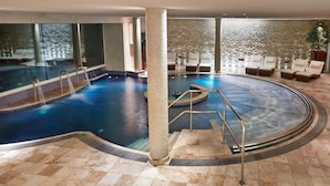 An indoor swimming pool with a circular design, surrounded by lounge chairs and a stone wall.