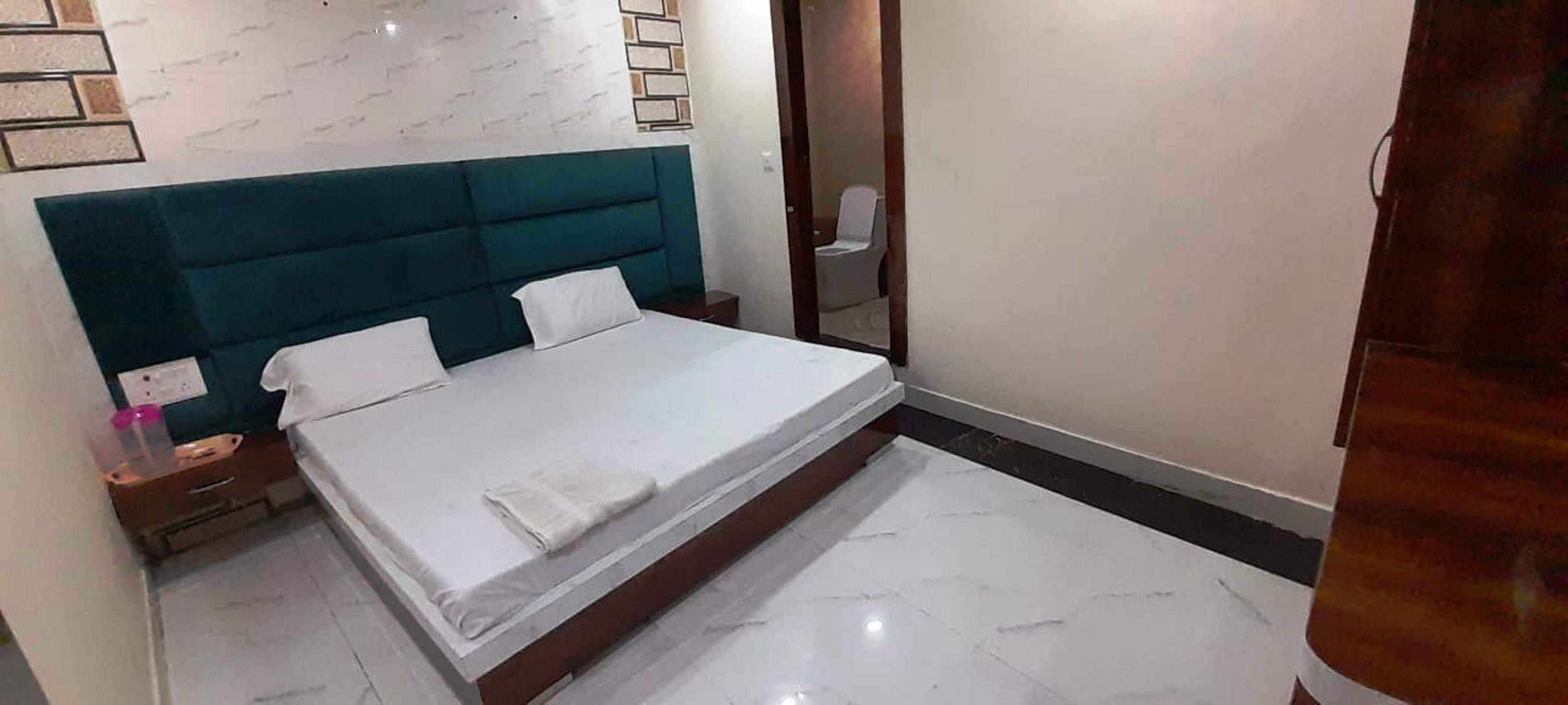 Een slaapkamer met een bed, een nachtkastje, een spiegel en een badkamedeur.