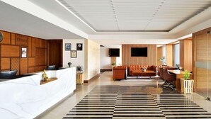 A modern reception area with a reception desk, seating area, and a large flat-screen TV. - Grandville Hotel Pousada (Barra de São Miguel)
