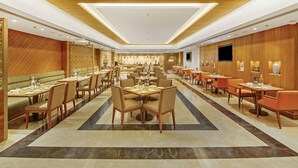 A spacious hotel dining area with multiple tables and chairs, a central seating area, and a television mounted on the wall. - Grandville Hotel Pousada (Barra de São Miguel)