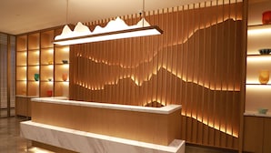 Bancada de recepção com tampo de mármore, painéis de madeira com desenhos iluminados e uma luminária pendente moderna.