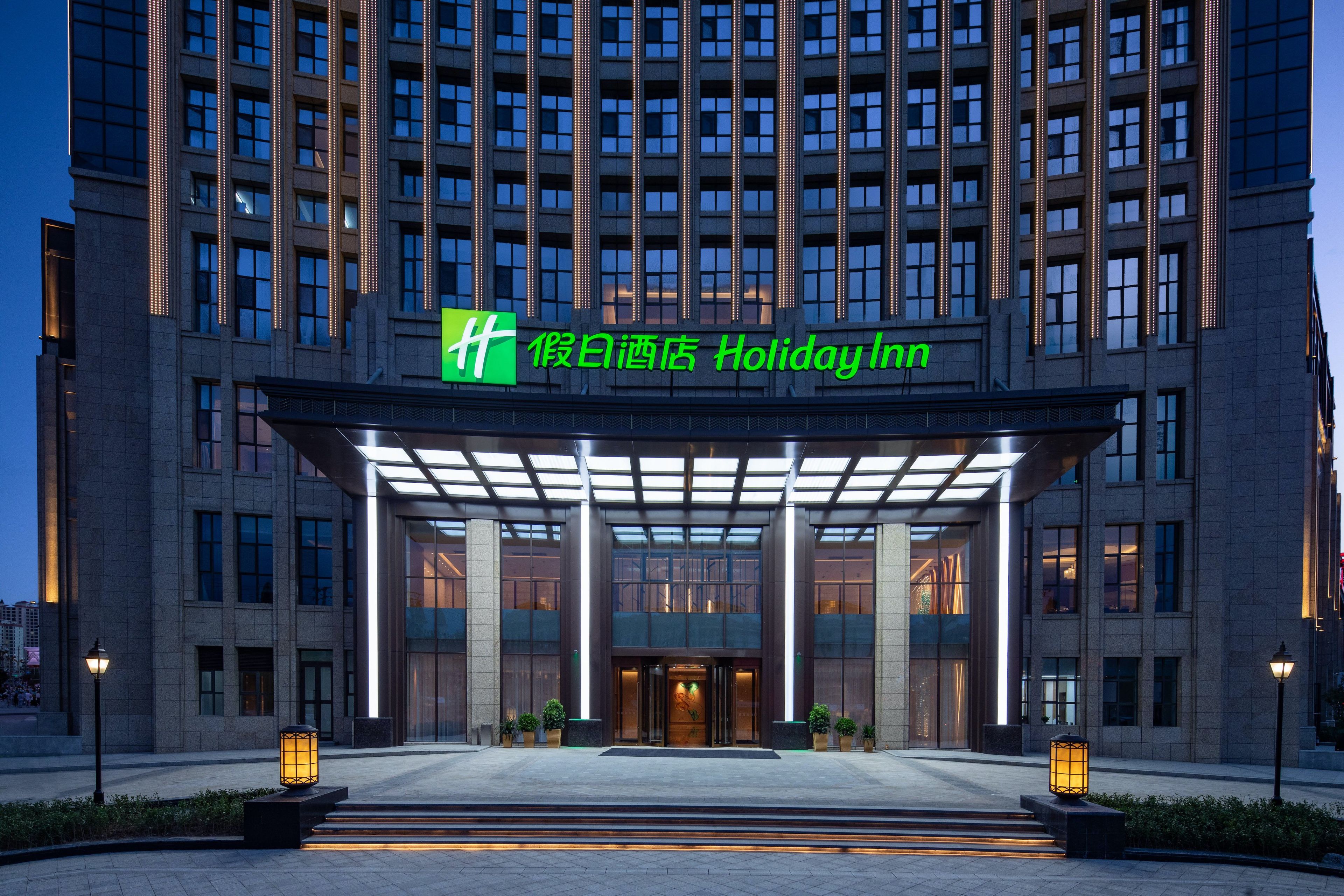 A hotel entrance with a modern design, featuring a prominent green sign above the entrance.