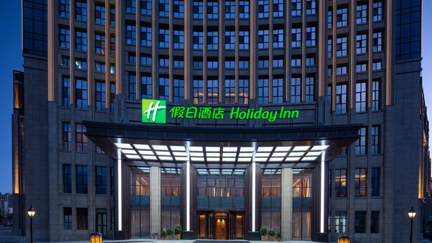 Der Eingang eines Holiday Inn Hotels mit modernem Design, gekennzeichnet durch eine auffällige grüne Beschilderung, einen überdachten Eingangsbereich und eine gut beleuchtete Fassade.