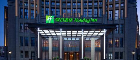 A hotel entrance with a modern design, featuring a prominent green sign above the entrance.