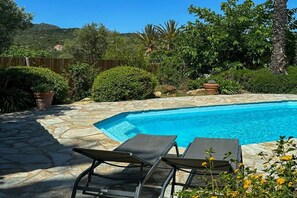 A swimming pool with stone tiles, surrounded by greenery and a wooden fence. - Villa in Monticello with swimming pool (MONTICELLO)