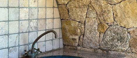 A bathroom with a stone wall, a tiled wall, and a blue sink.