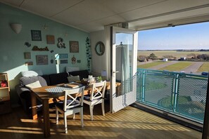 Ein Balkon mit Blick auf eine ländliche Landschaft, ein Essbereich mit Tisch und Stühlen sowie ein Wohnzimmer mit Sofa und Wanddekorationen.