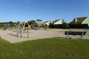 Ein Spielplatz mit verschiedenen Spielgeräten, einer Bank und Häusern im Hintergrund.