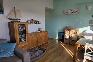 Ein Wohnzimmer mit Holzschrank, einer Couch, einem kleinen Modellboot und einem Bücherregal.