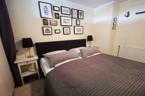 Ein Schlafzimmer mit einem Bett, zwei Nachttischen, einer Wand mit gerahmten Bildern und einer Tür mit einem Symbol.