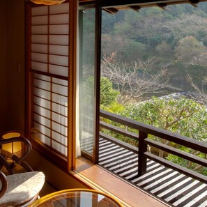 A room with a view of a forested area through a large window with a wooden frame and a sliding door. - Shimoda Rendaiji Onsen Seiryuso (Shimoda)