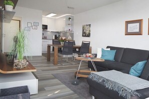 A modern living room with a black sofa, a coffee table, and a dining area with a wooden table and chairs. - Holiday apartment with 1 bedroom (Glücksburg- Schausende)