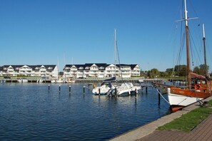 Ein Yachthafen mit vertäuten Booten, eine Reihe weißer Gebäude mit dunklen Dächern und ein klarer, blauer Himmel.