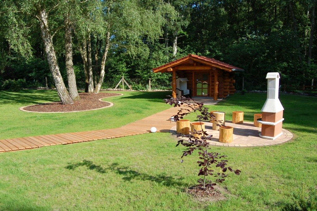 Una cabaña de madera con chimenea, rodeada por un jardín circular con un sendero de madera que lleva a ella.