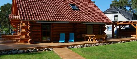 En hytte med tagsten, en træterrasse og en sti af sten, der fører til indgangen.