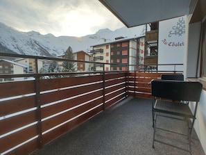 A balcony with a view of snow-covered mountains, a wooden railing, and a chair. - L'Orée 12 Appartement/Fewo 4-Bettwohnung by Interhome (Saas-Fee)