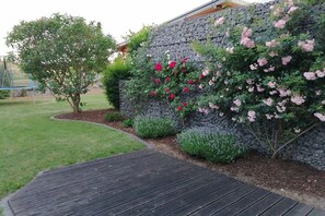 Ein Garten mit einer Steinsäule, blühenden Pflanzen, einem Baum und einer Holzterrasse.