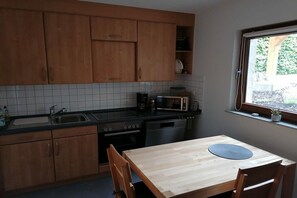 Eine kompakte Küche mit Holzausstattung, einer Mikrowelle, einem Spülbecken und einem Fenster mit Blick auf Grünflächen.