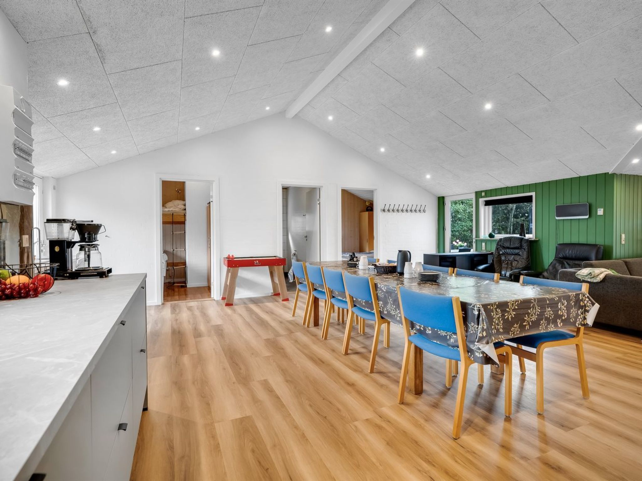 Un comedor amplio con una mesa larga, sillas azules y una zona de cocina con una máquina de café.
