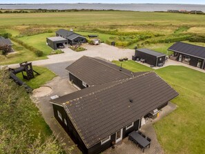 A modern building with a large patio area, surrounded by open fields and a body of water in the background. - "Nahuel" - 300m to the fjord by Interhome (Vinderup)