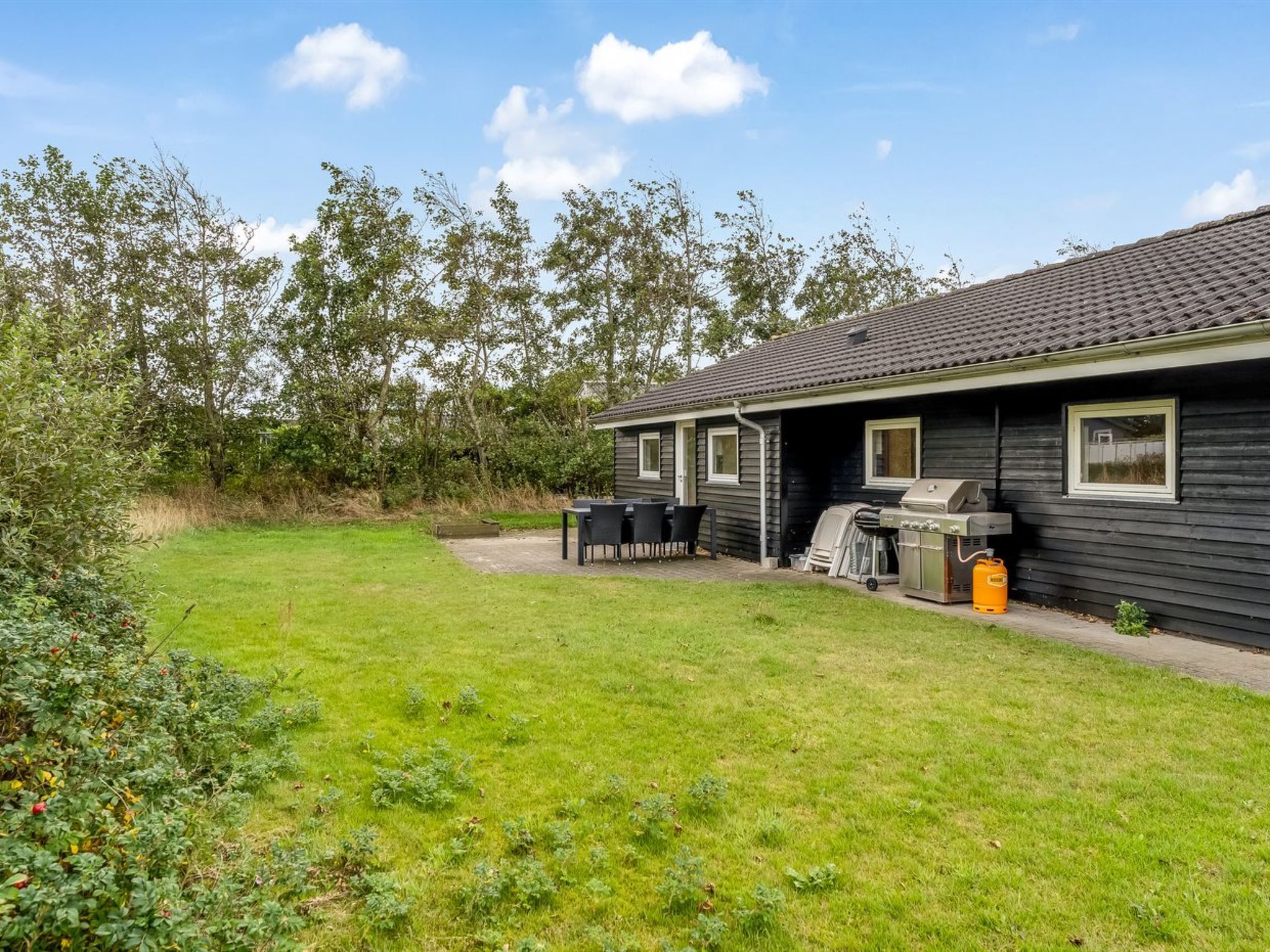 A single-story house with a patio area, a barbecue grill, and a small table with chairs.