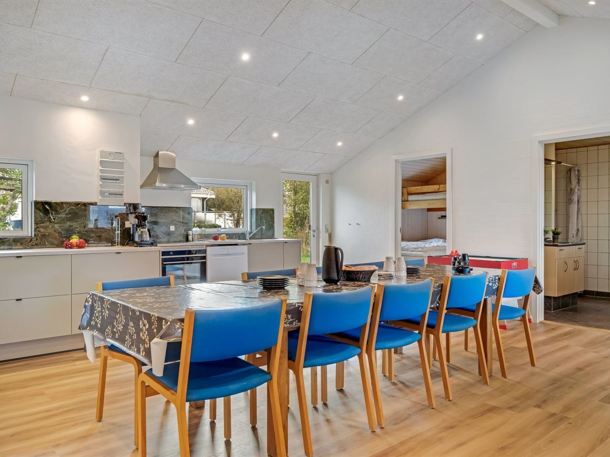 Una cocina moderna con comedor, que presenta una mesa grande con sillas azules, piso de madera y vista por la puerta abierta.