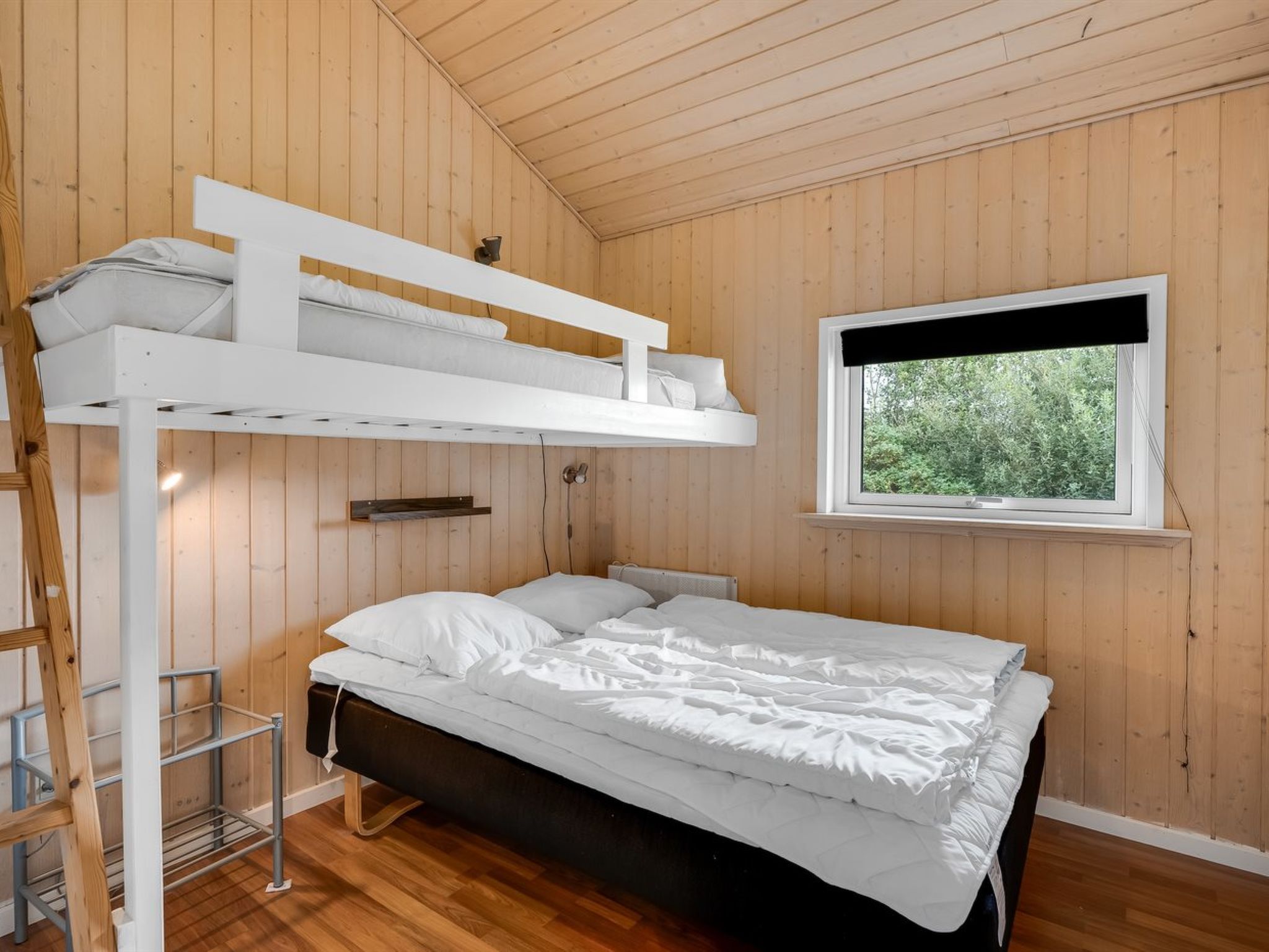 Ein Stockbett mit weißem Kopfteil und einem Fenster mit schwarzem Rollo.
