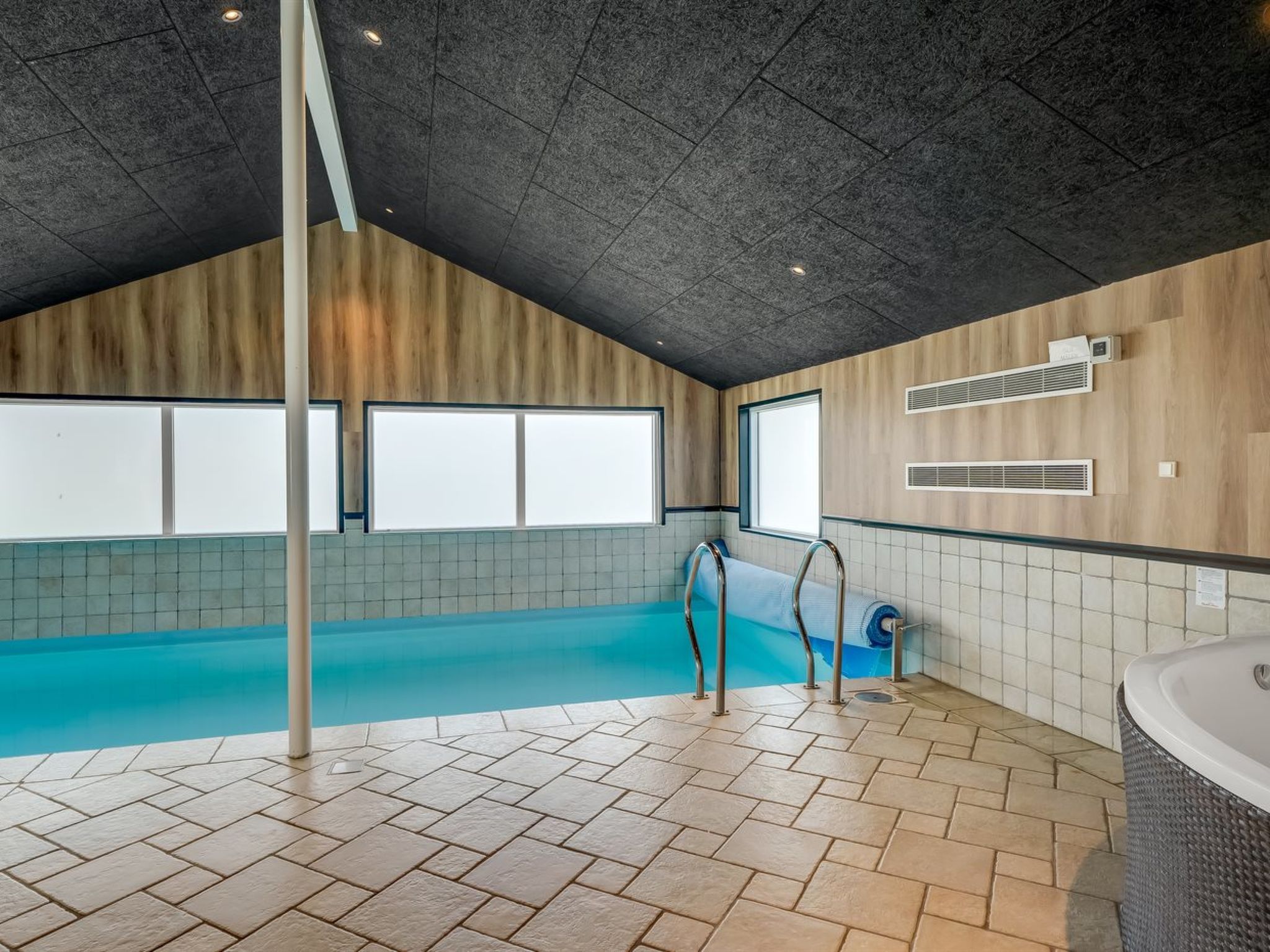An indoor swimming pool with a wooden ceiling and tiled walls.