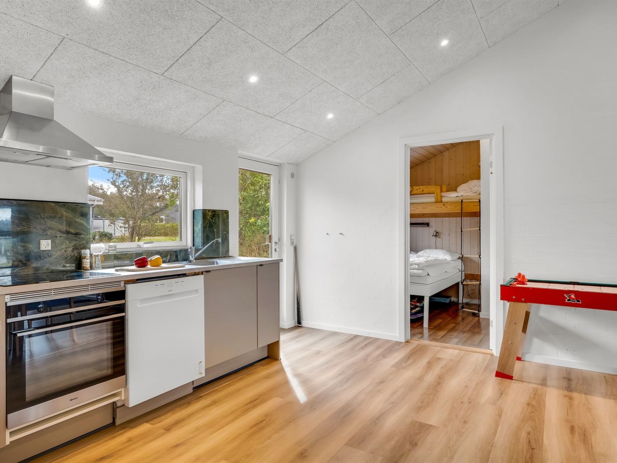 A modern kitchen with a dishwasher, oven, and a window with a view of greenery.