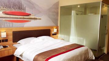 A hotel room with a bed, a nightstand with a phone, a glass shower enclosure, and a mural on the wall.