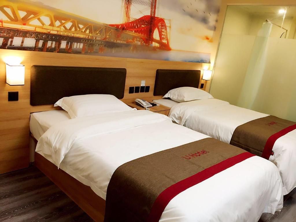 Ein Hotelzimmer mit zwei Betten, einem Holzkopfstück, einem Nachttisch und einer Wandlampe.