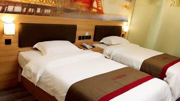 A hotel room with two beds, a wooden headboard, a nightstand, and a wall-mounted lamp.