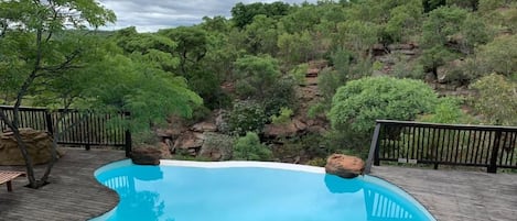 A swimming pool with a wooden deck and a view of a rocky hillside.