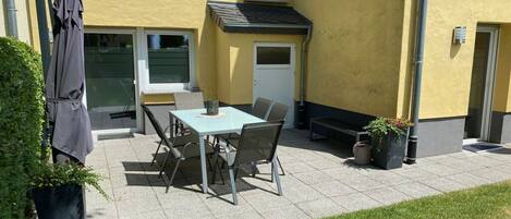 An outdoor patio with a table and chairs, a covered bench, and potted plants.