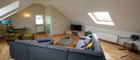 A modern loft-style living room with a large gray sectional sofa, a small coffee table, and a flat-screen TV.