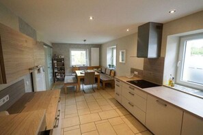 A modern kitchen with a dining area, built-in shelving, and a large window. - Holiday home Moseltraum (Dieblich)