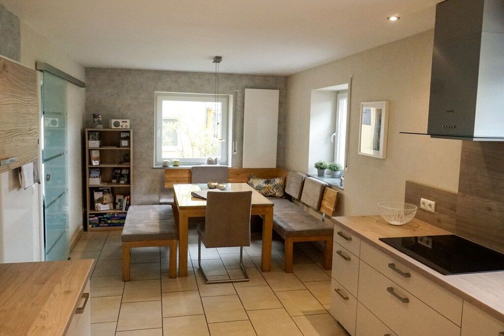A modern kitchen with a dining area, built-in shelving, and a large window.