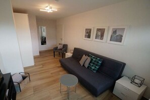 A modern living room with a sofa, a small round table, and a white nightstand. There are framed pictures on the wall and a door leading to another room. - Holiday home Moseltraum (Dieblich)