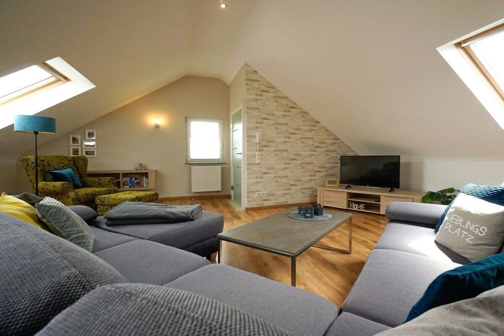 Eine moderne Loftswohnung mit schrägem Dach, einer Sofagarnitur, einem Fernseher und einem kleinen Tisch.