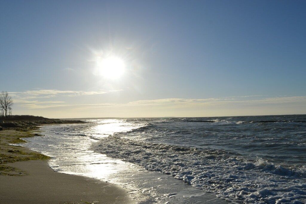 A beach with waves, a clear sky, and the sun shining.