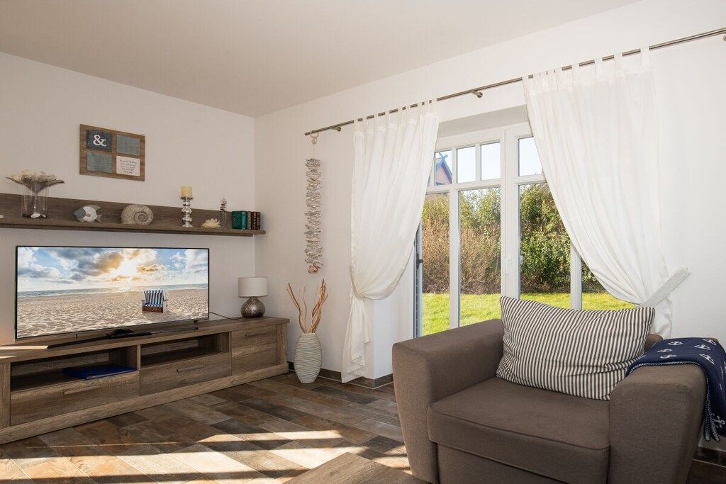 A living room with a flat-screen TV, a sofa, a wooden entertainment unit, and a large window with curtains.