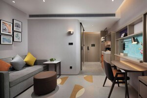 Un interior moderno con un sofá, un reposapiés y un escritorio con una silla. Hay cuadros en la pared y una pequeña mesa con una planta.